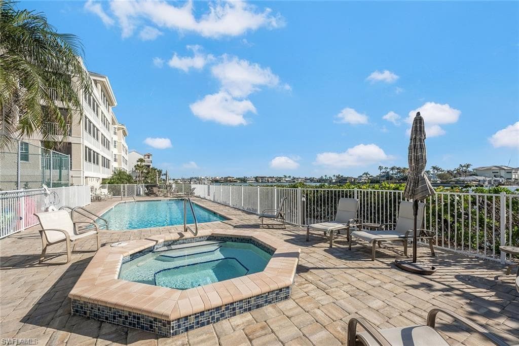 Paver patio featuring a swimming pool, integrated spa, and white perimeter fencing