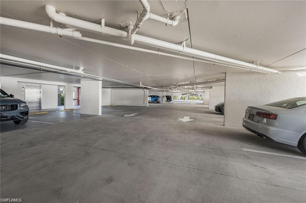 Underground parking garage featuring concrete flooring, exposed overhead piping, and designated parking spaces