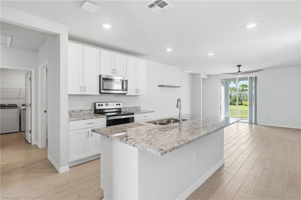 Kitchen featuring white cabinetry, stainless steel appliances, granite countertops, an island with an undermount double sink, and wood-finish flooring