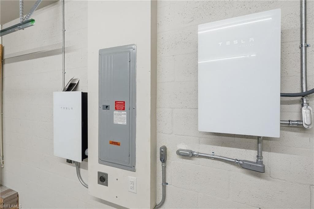 Two Tesla Powerwall units with an electrical panel and conduit systems on a concrete block wall