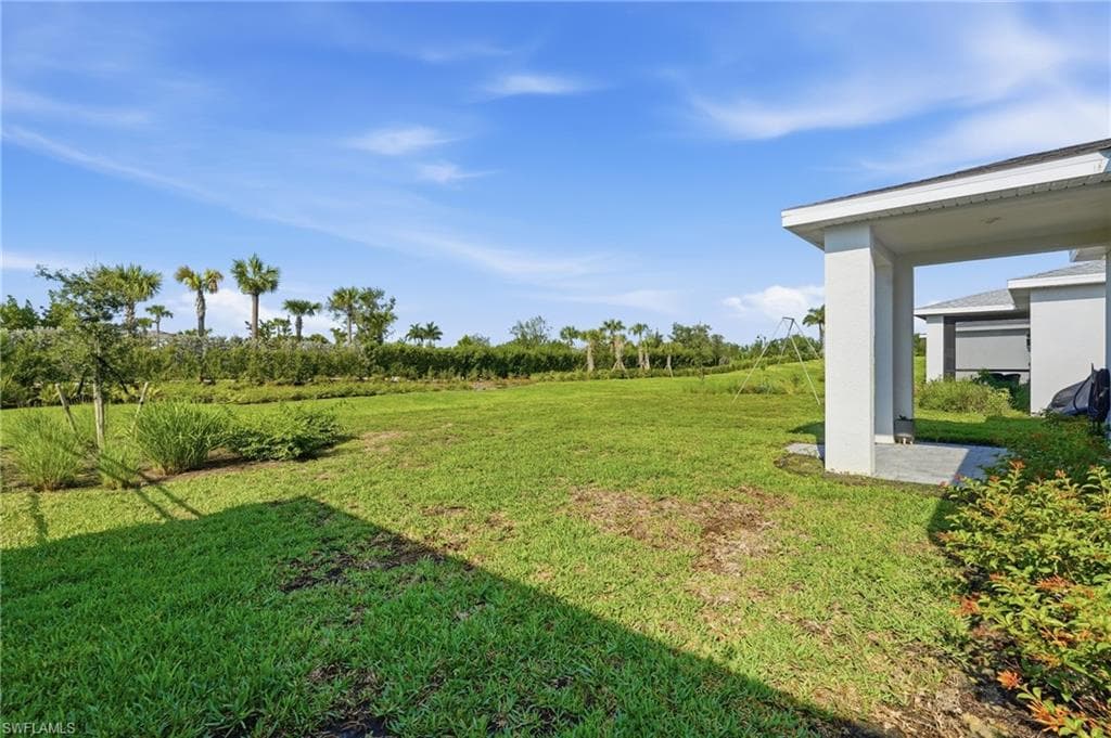 Expansive green lawn with a covered patio area, surrounded by lush landscaping and mature palm trees