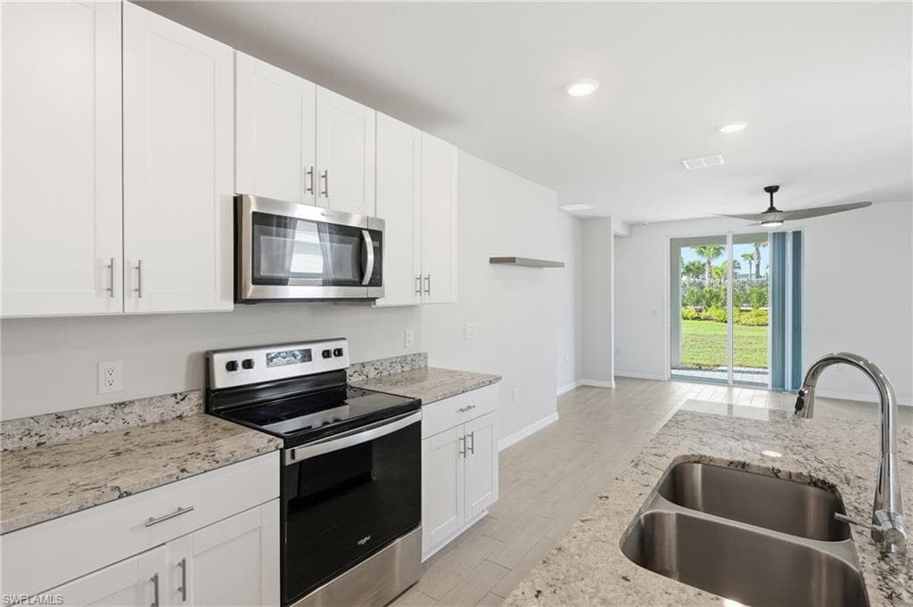 Modern kitchen featuring white cabinetry, stainless steel appliances, speckled countertops, and a double basin sink with a high-arch faucet