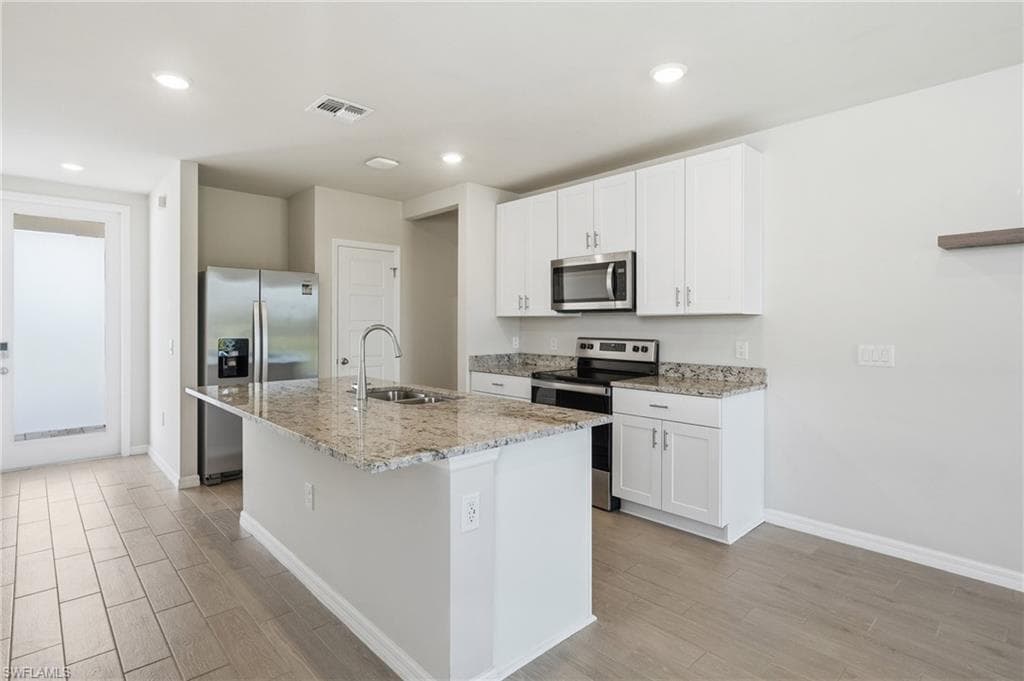 Modern kitchen featuring an island with a stainless steel sink, granite countertops, white cabinetry, stainless steel appliances, and wood-finish flooring