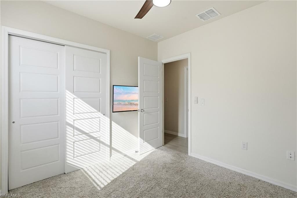 Bedroom featuring light gray carpet flooring, white paneled doors, and a ceiling fan with integrated lighting