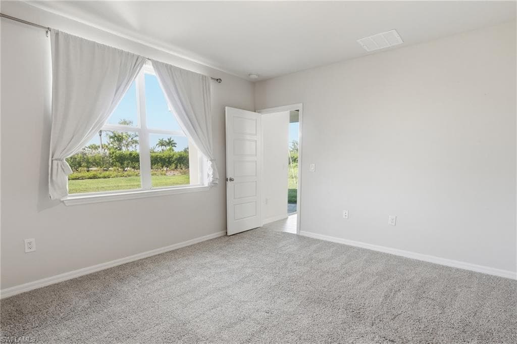 Bedroom featuring a large multi-pane window, neutral gray walls, light gray carpet, white trim, and a white interior door with horizontal paneling