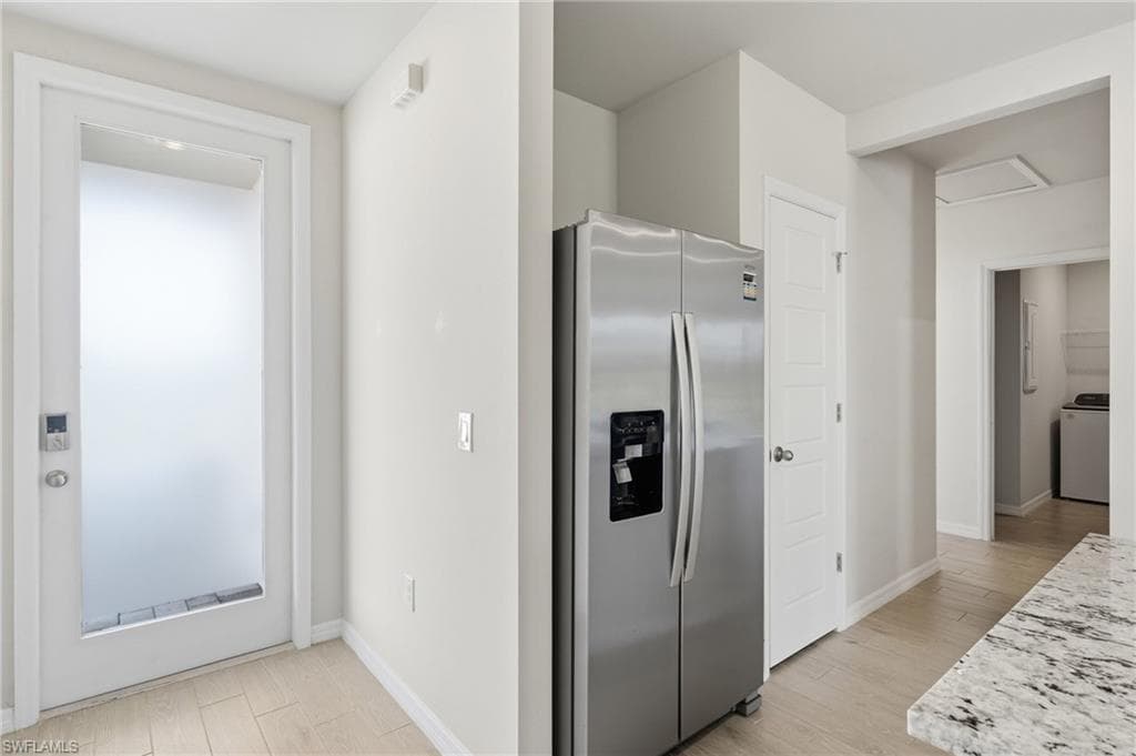 Stainless steel side-by-side refrigerator, white paneled doors, and light wood-finish flooring