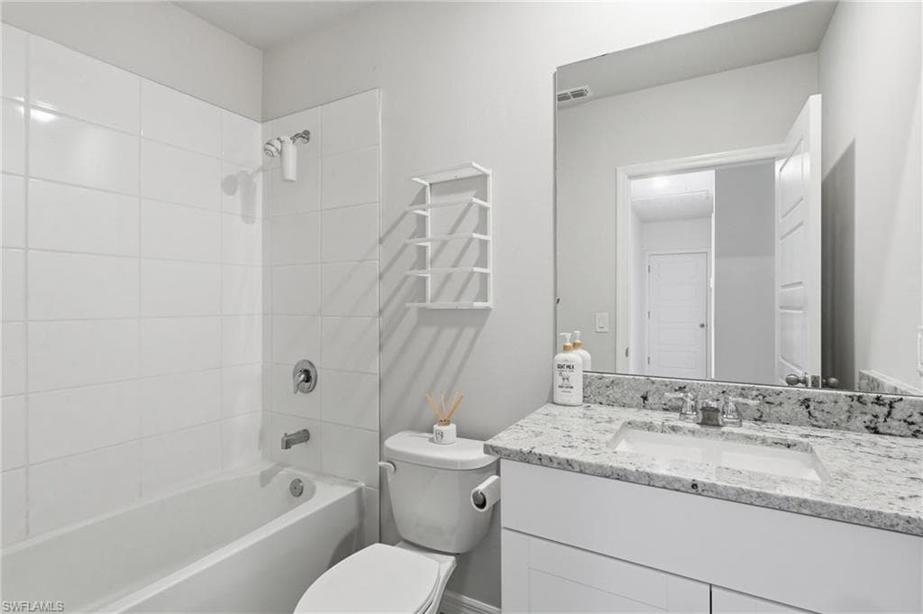 Bathroom featuring a white bathtub with subway tile surround, polished chrome fixtures, and a vanity with a light-colored stone countertop