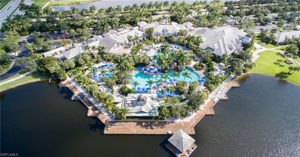 Expansive outdoor amenity area featuring a large lagoon-style swimming pool, surrounding lounge seating, mature palm trees, multiple buildings with varied rooflines, and waterfront access with a dock and covered gazebo