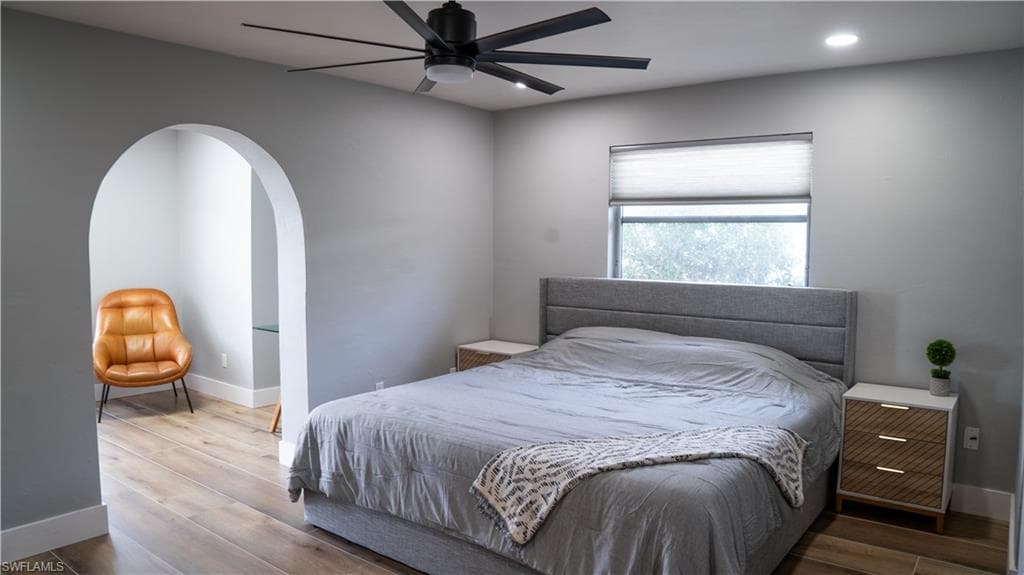 Bedroom featuring an arched doorway, wood-finish flooring, a contemporary ceiling fan, recessed lighting, and a window with a cellular shade