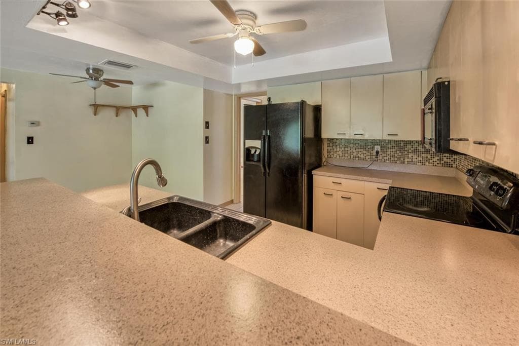 Kitchen with sink, black appliances, a raised ceiling, decorative backsplash, and cream cabinetry