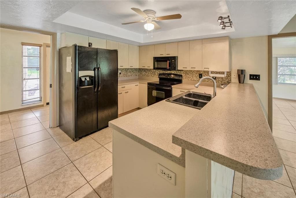 Kitchen with sink, black appliances, kitchen peninsula, a raised ceiling, and cream cabinetry