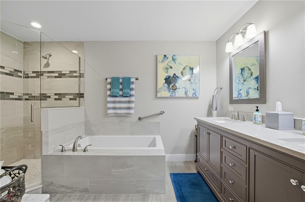 Bathroom featuring a double vanity with stone countertop, tile-surround soaking tub with deck-mounted faucet, and a glass-enclosed shower with tiled walls and decorative band