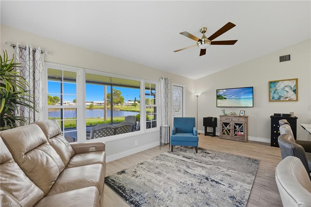 Expansive living area featuring large windows with water views, wood-finish flooring, a vaulted ceiling, and a ceiling fan