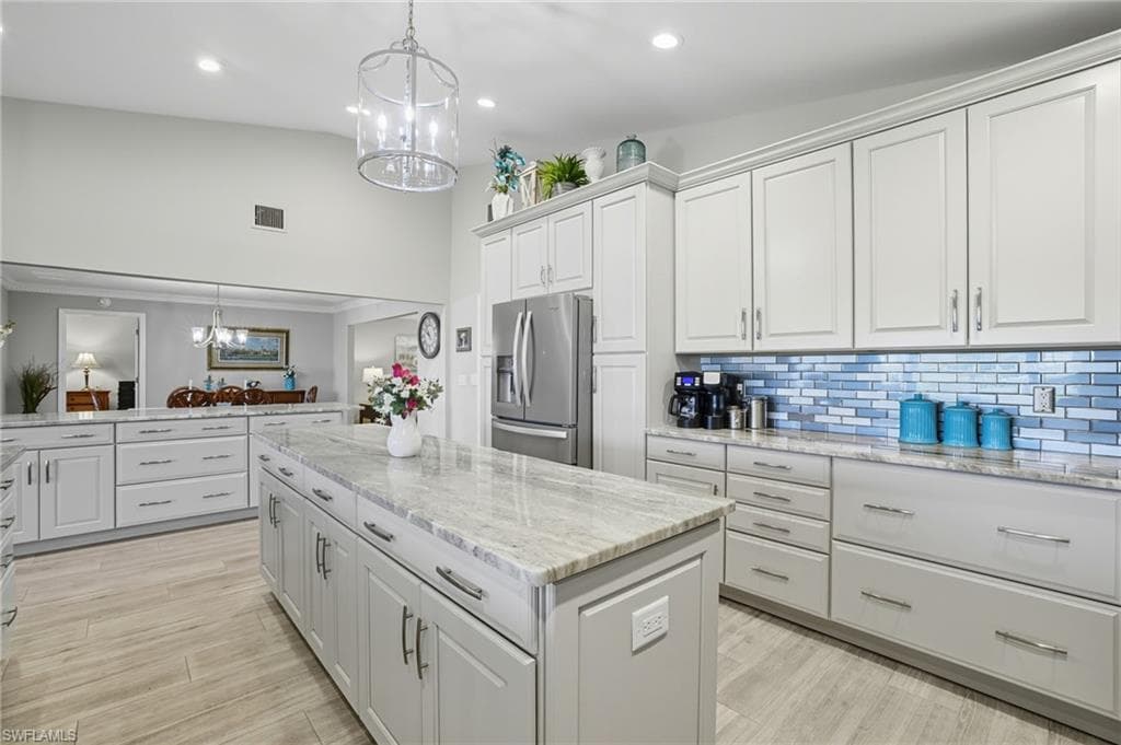 Spacious kitchen featuring an expansive center island with stone countertop, abundant white cabinetry, stainless steel appliances, and wood-finish flooring