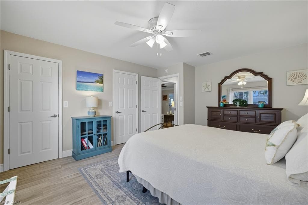 Bedroom featuring wood-finish flooring, a ceiling fan with integrated lighting, multiple paneled doors, and a decorative area rug