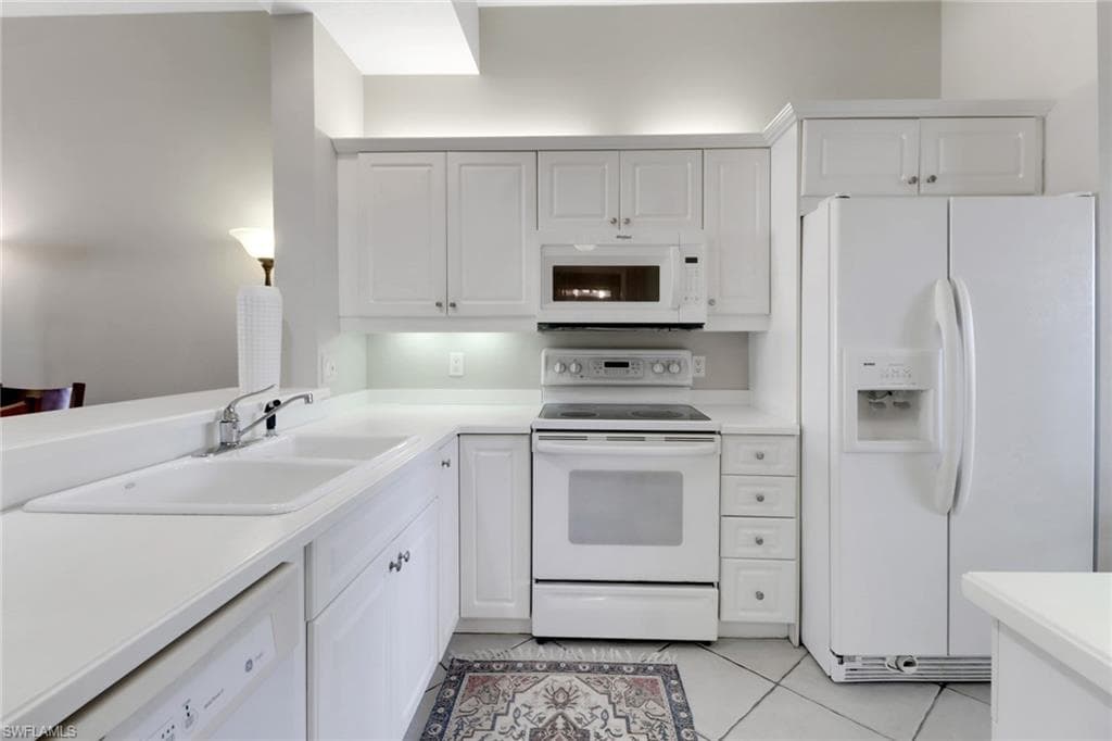 Kitchen with white appliances, light tile patterned flooring, light countertops, and white cabinets
