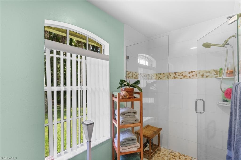 Bathroom featuring a walk-in shower with clear glass enclosure and pebble flooring, accented by a decorative mosaic tile band