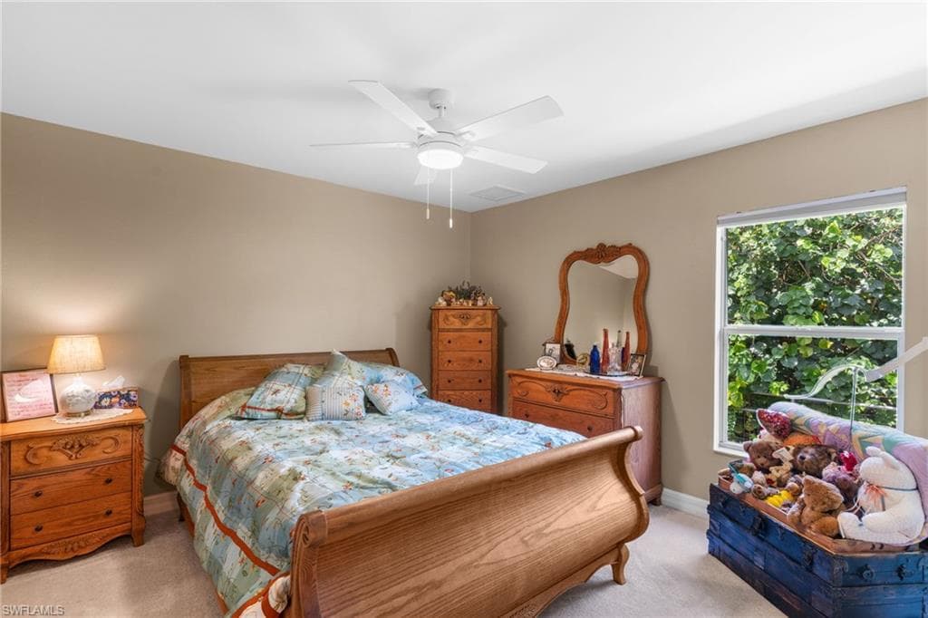 Bedroom featuring neutral wall paint, carpet flooring, a ceiling fan with integrated lighting, and a large window overlooking lush greenery
