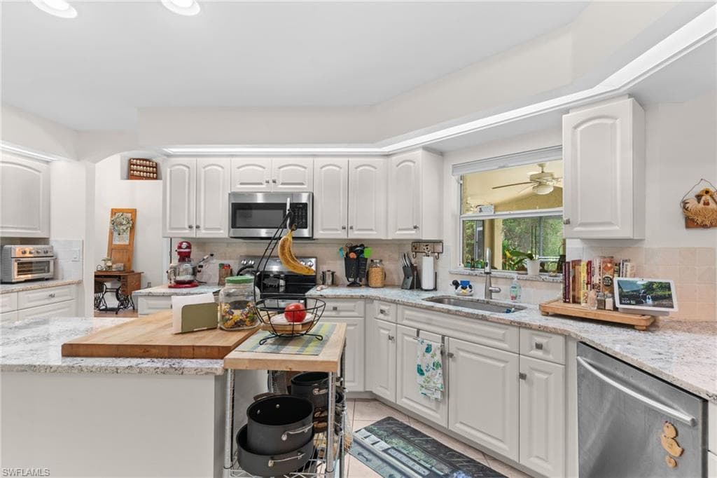 Kitchen featuring white cabinetry, light-toned countertops, tile backsplash, and stainless steel appliances