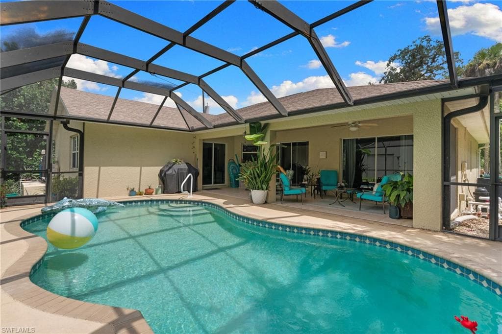 Screened-in pool deck featuring a freeform swimming pool with a mosaic tile border, an expansive covered patio, and direct access to the interior through sliding glass doors