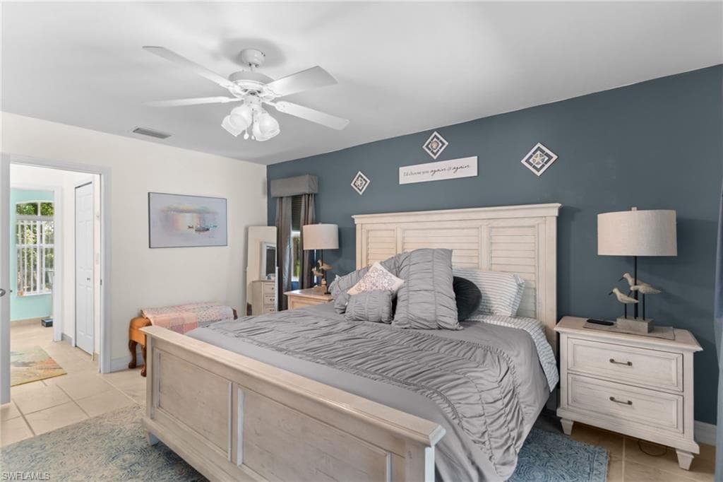 Bedroom featuring a light-toned wood-finish bed frame and headboard, ceiling fan, and tile flooring