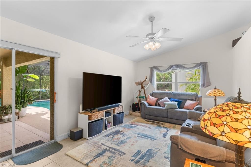 Living area featuring vaulted ceilings, a ceiling fan with light fixture, tile flooring, and sliding glass doors opening to a covered patio and pool area