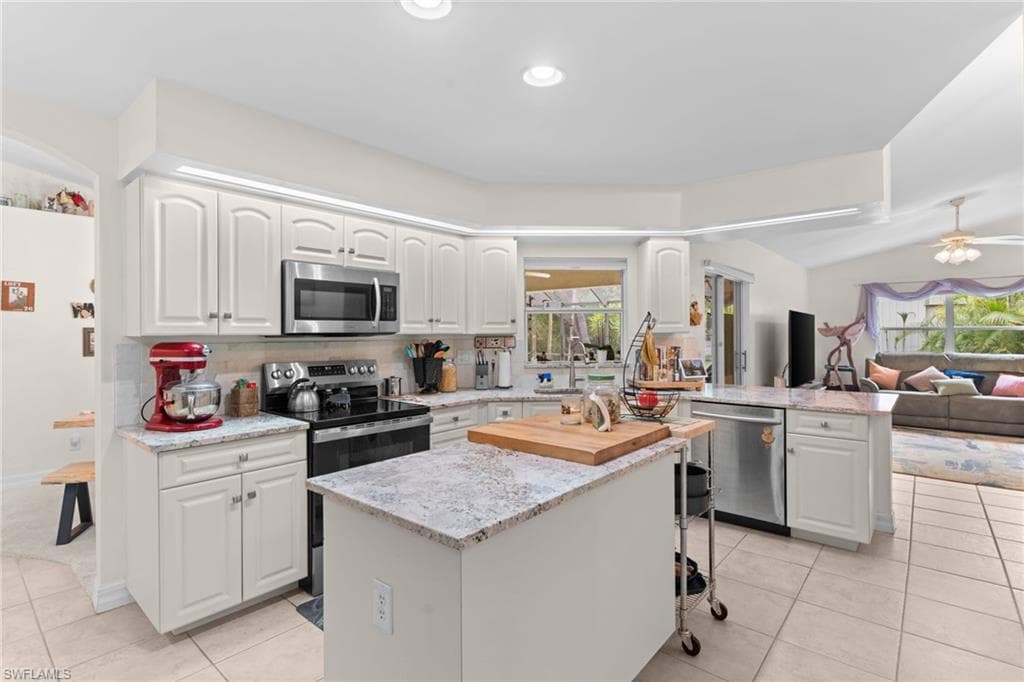 Bright kitchen featuring white cabinetry, stainless steel appliances, granite countertops, and tile flooring
