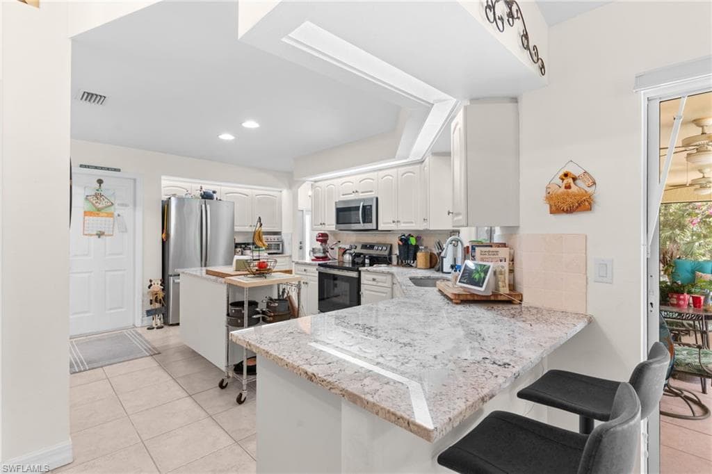 Kitchen featuring white cabinetry, stainless steel appliances, and a granite-finish countertop with breakfast bar seating