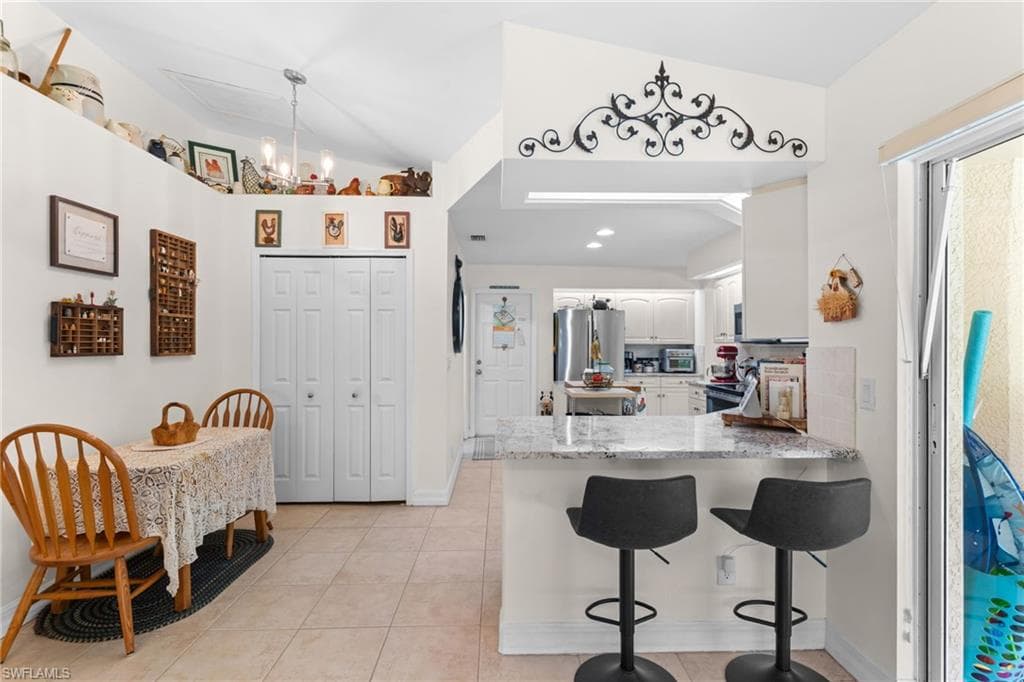 Kitchen and dining area featuring vaulted ceilings, tile flooring, a breakfast bar with granite-finish countertop, and a sliding glass door