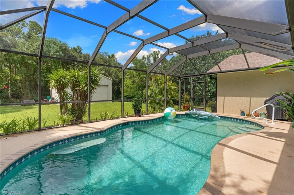 Screened enclosure encompassing a freeform swimming pool with integrated steps, surrounded by a paved deck