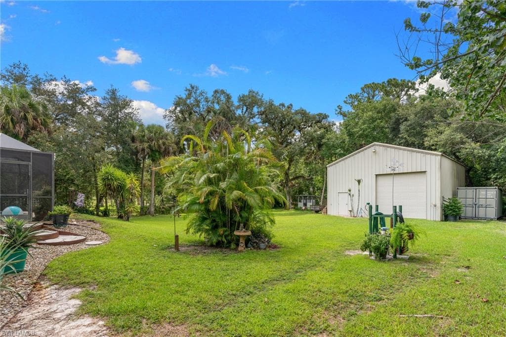 Expansive green lawn featuring a large metal outbuilding with a roll-up door, surrounded by mature trees and tropical foliage