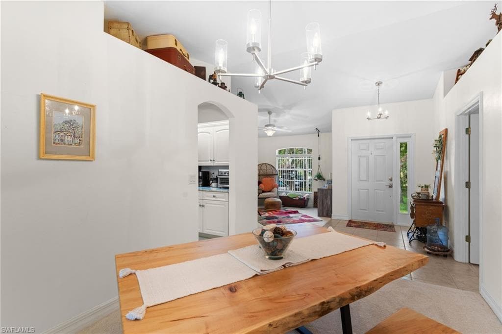 Natural wood-finish dining table with modern chandelier, high ceilings, arched kitchen entry, and tiled flooring