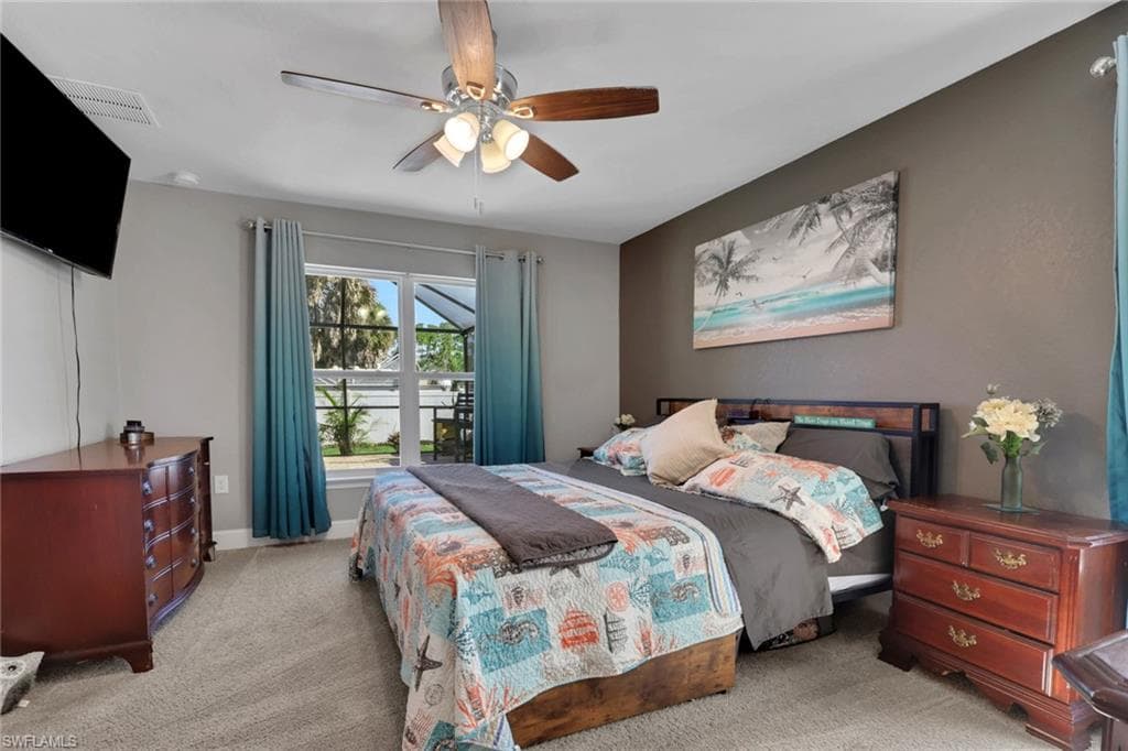Carpeted bedroom featuring a ceiling fan with light kit, a window with outdoor access, and a contrasting accent wall