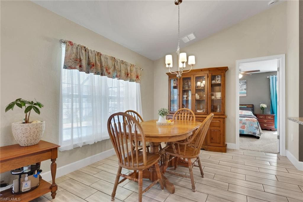Vaulted ceiling dining area featuring tile flooring, a window with blinds, and a multi-light chandelier