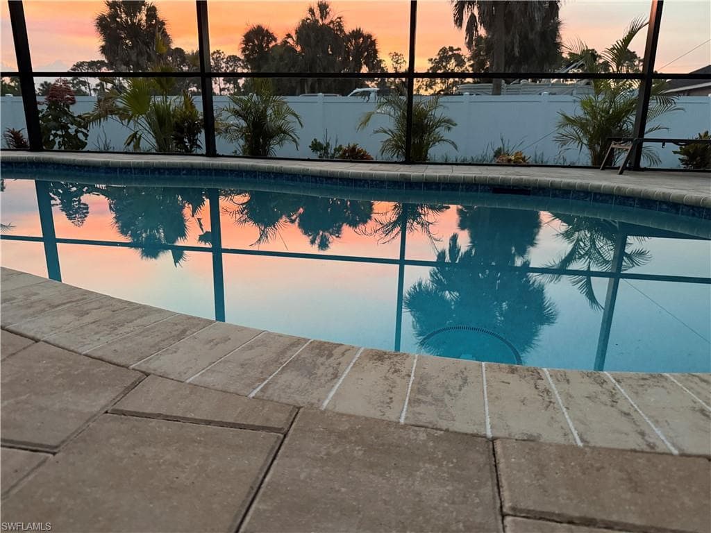 Screened swimming pool featuring a tiled waterline, paver decking, and surrounding tropical landscaping