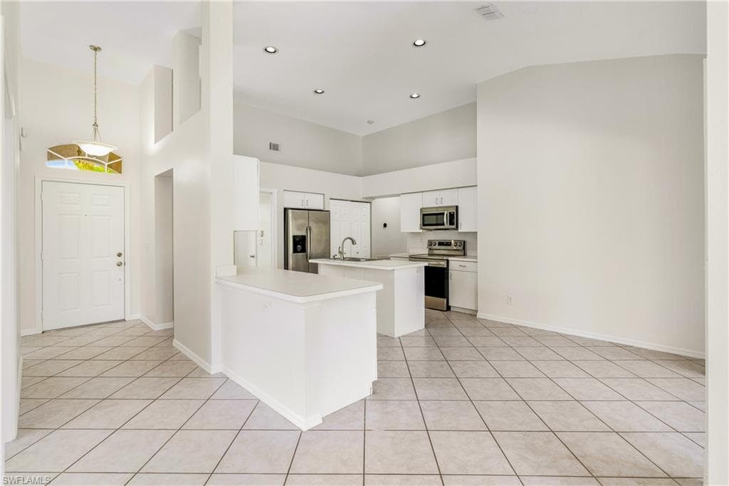 Open concept living space featuring a kitchen with white cabinetry, stainless steel appliances, and a central island.
