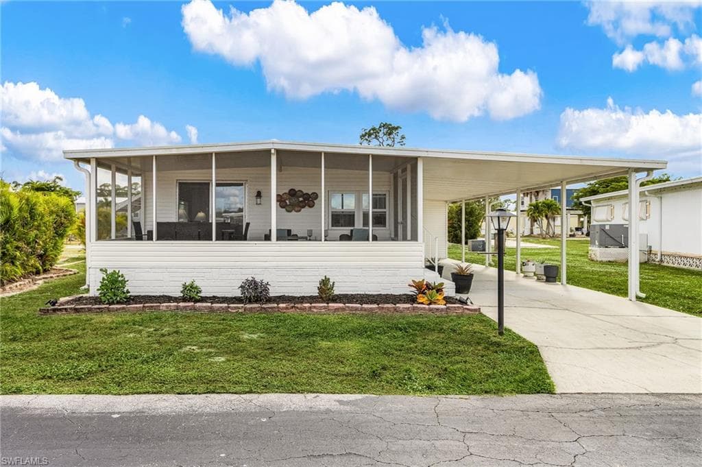 White siding residence featuring a screened-in porch, covered carport, concrete driveway, and a front garden bed with dark mulch