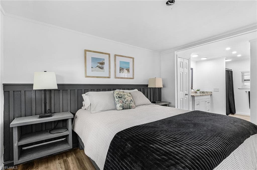 Bedroom featuring wood-finish flooring, a paneled accent wall, and crown molding