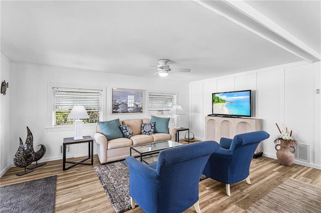 Living area featuring wood-finish flooring, white paneled walls, and a ceiling fan