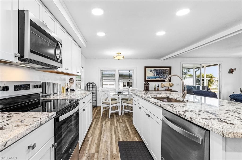 Kitchen featuring an expansive island with a stainless steel sink and faucet, white cabinetry, granite countertops, stainless steel appliances, and wood-finish flooring