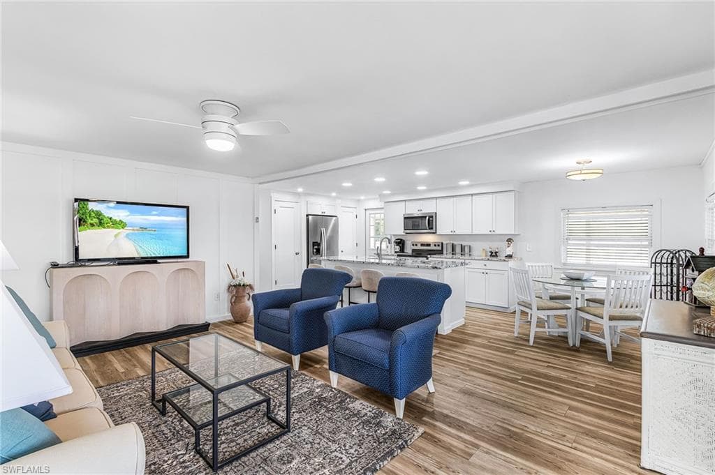 Open-concept living space featuring wood-finish flooring, recessed lighting, a modern ceiling fan, white cabinetry, and stainless steel appliances
