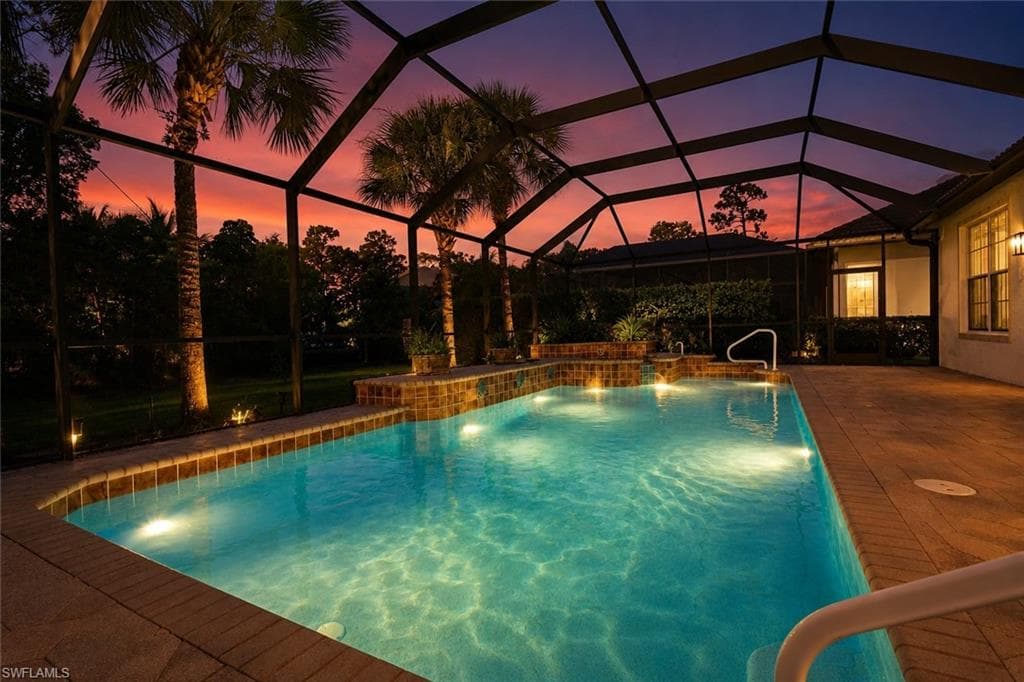 Screened outdoor swimming pool featuring submerged lighting, integrated water features, and a brick paver deck