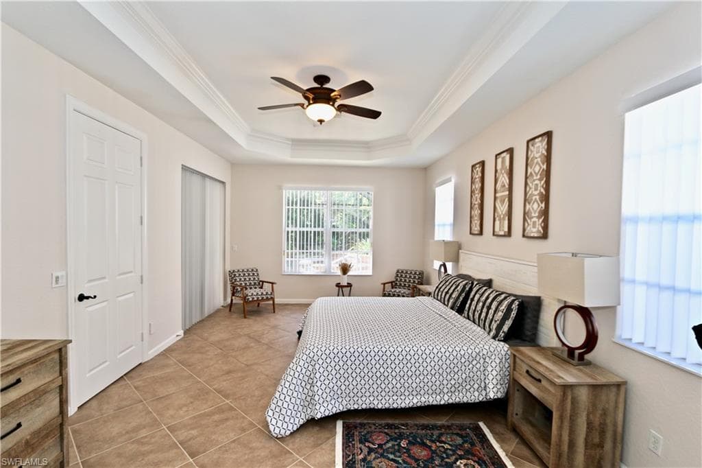 Spacious bedroom featuring a tray ceiling with crown molding, ceiling fan, and tile flooring
