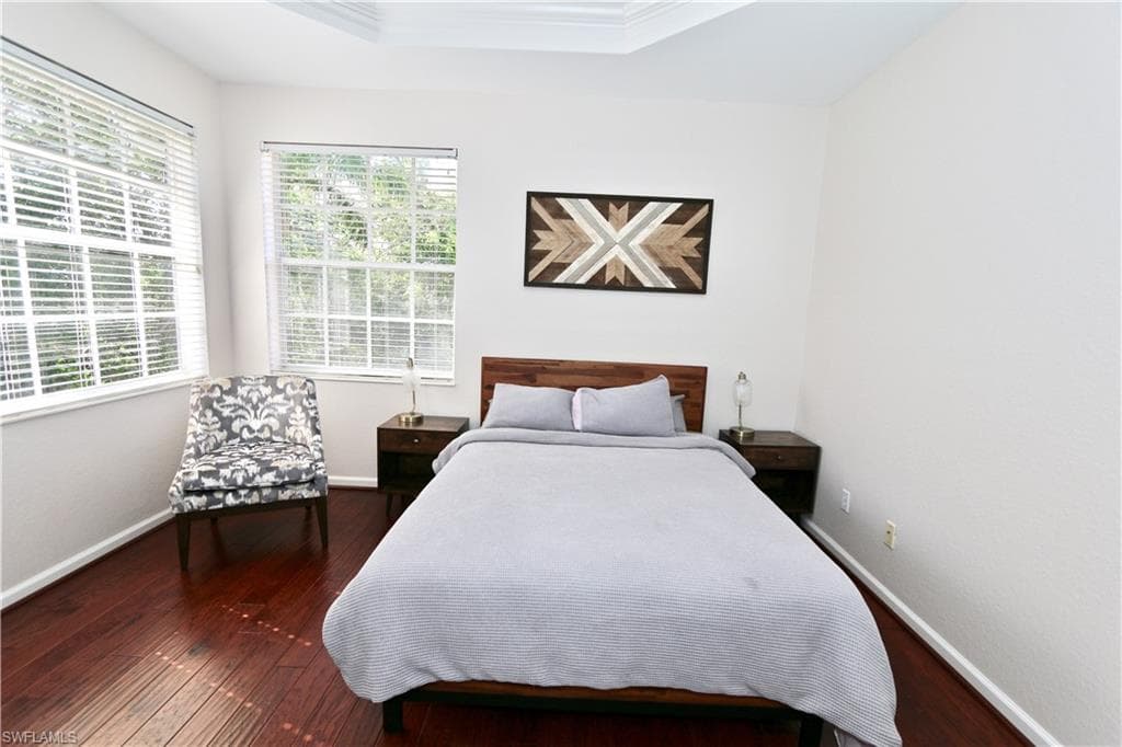 Spacious room featuring rich wood-finish flooring, multiple windows with blinds, a tray ceiling, and neutral wall paint