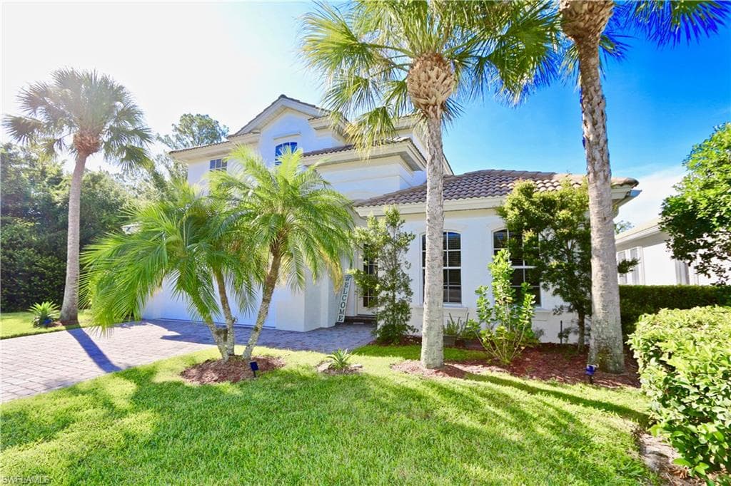 Stucco exterior architecture featuring a tiled roof, arched windows, and a paver driveway