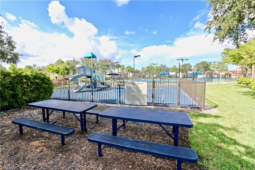 Outdoor recreational area featuring a playground with slides, multiple tennis courts with fencing, and two picnic tables with benches