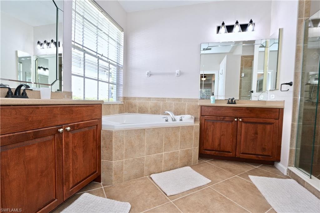 Bathroom featuring a corner soaking tub, dual wood-finish vanities with light countertops, and a tiled shower enclosure