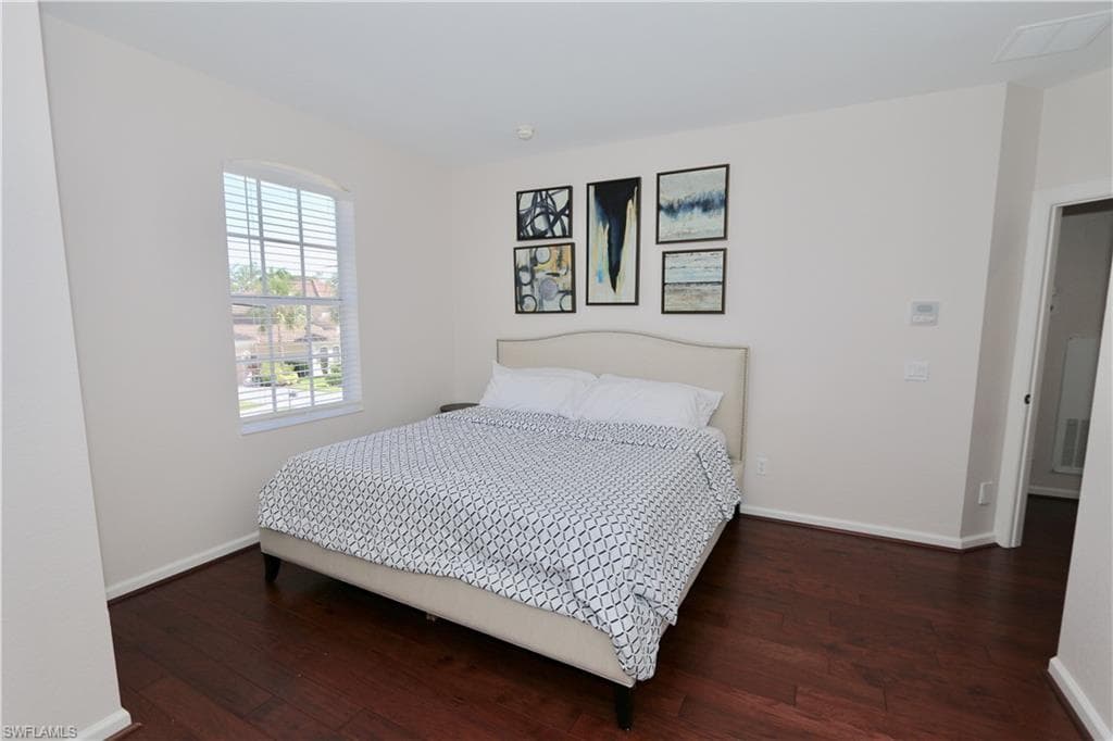 Bedroom featuring wood-finish flooring, an arched window with blinds, and light-toned walls