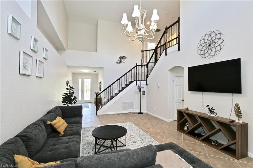 Spacious two-story living area featuring high ceilings, a grand staircase with dark wood railings, and tile flooring