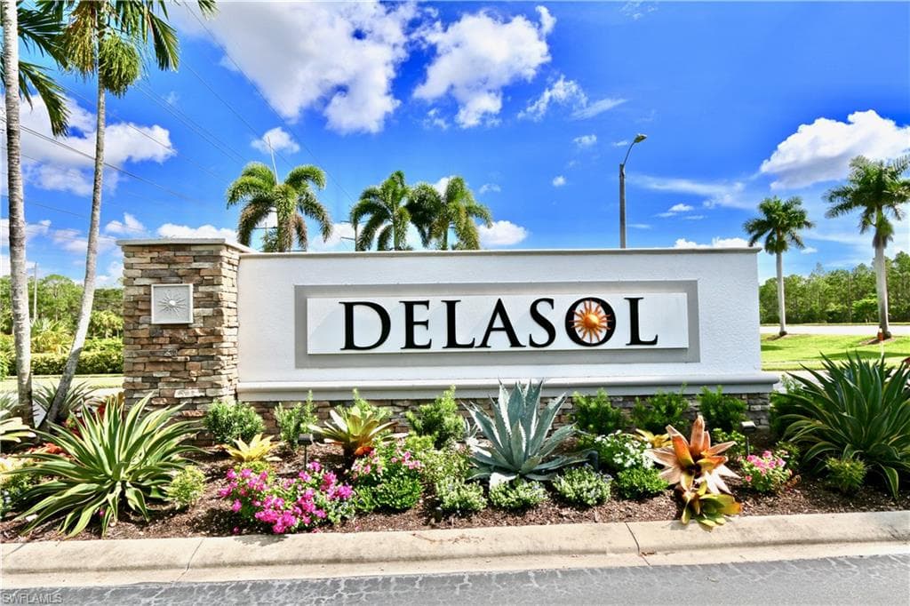 Monument sign featuring stacked stone and white stucco, framed by tropical landscaping, palm trees, and a clear blue sky